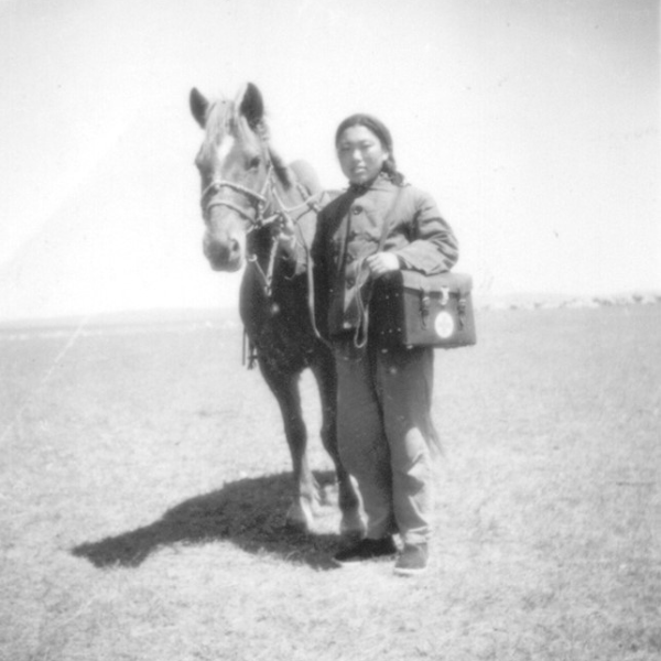 Black and white photo of a young Asian lady standing next to a horse and carrying a doctor bag on her shoulder